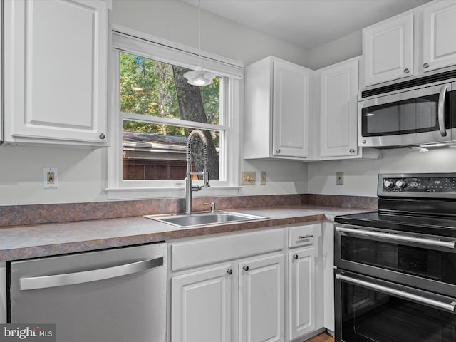 kitchen with sink, appliances with stainless steel finishes, decorative light fixtures, and white cabinetry