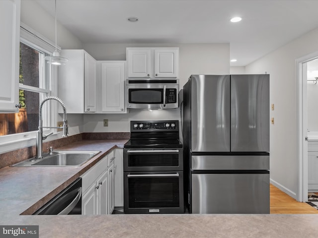 kitchen with light hardwood / wood-style flooring, hanging light fixtures, sink, white cabinetry, and appliances with stainless steel finishes