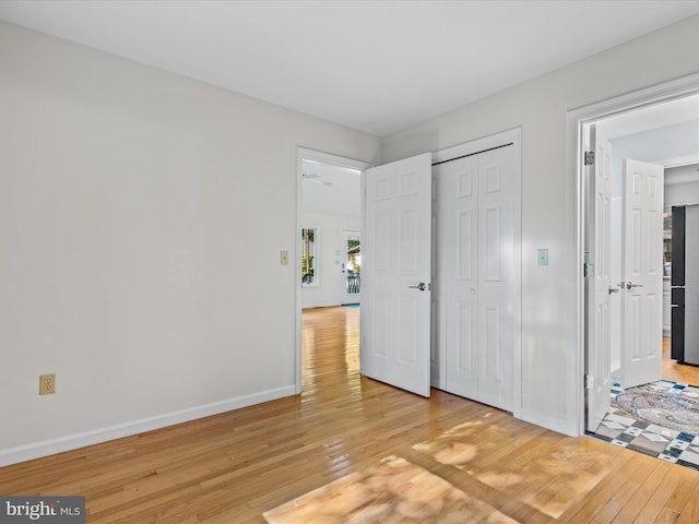 unfurnished bedroom featuring a closet, light hardwood / wood-style floors, and stainless steel refrigerator