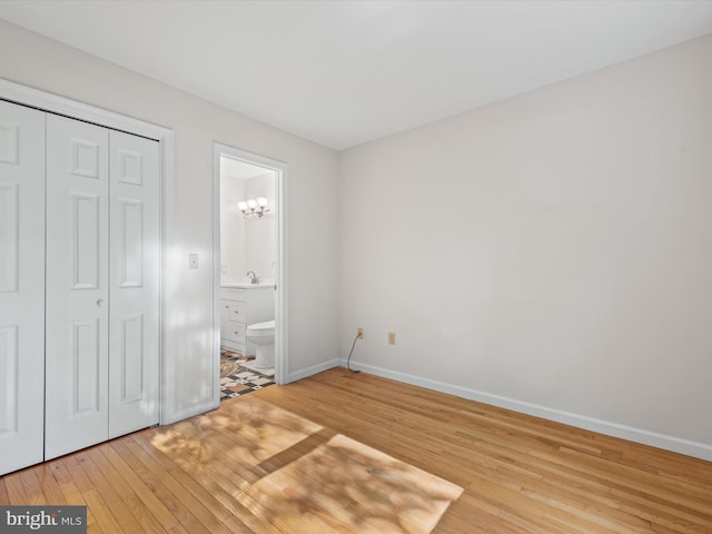 unfurnished bedroom featuring sink, light wood-type flooring, a closet, connected bathroom, and an inviting chandelier