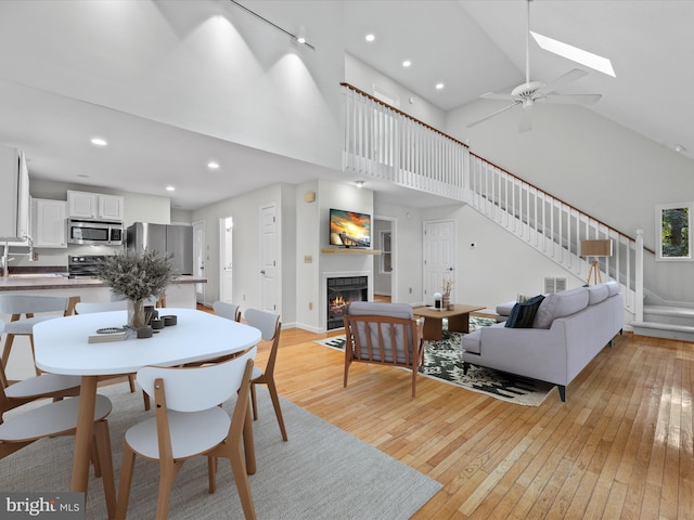 dining space featuring ceiling fan, high vaulted ceiling, a skylight, light hardwood / wood-style floors, and sink