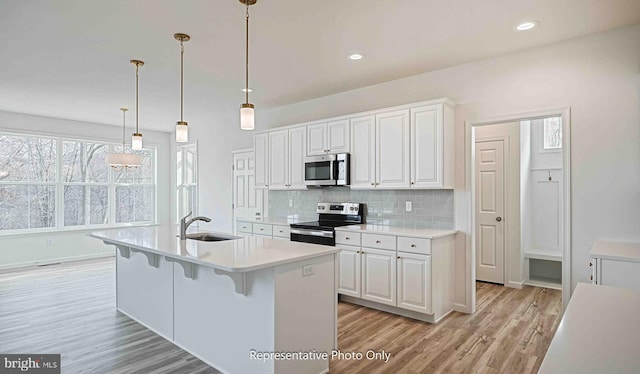 kitchen with sink, a kitchen island with sink, white cabinetry, stainless steel appliances, and light wood-type flooring