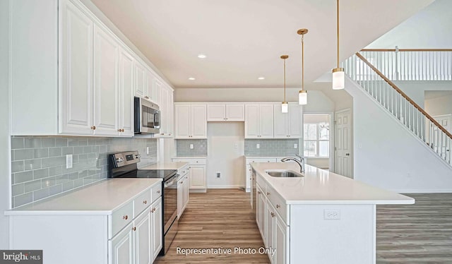 kitchen featuring wood-type flooring, white cabinetry, a center island with sink, and appliances with stainless steel finishes