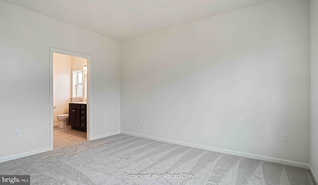 unfurnished bedroom featuring ensuite bath and light colored carpet