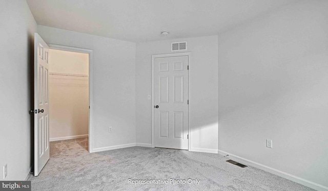 unfurnished bedroom featuring light carpet, a walk in closet, and a closet