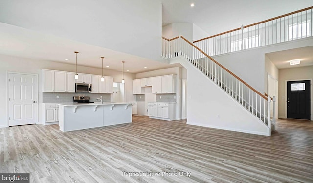 kitchen with light hardwood / wood-style floors, white cabinetry, stainless steel appliances, a high ceiling, and a kitchen island with sink