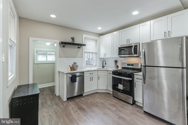 kitchen with white cabinets, sink, light hardwood / wood-style flooring, backsplash, and appliances with stainless steel finishes