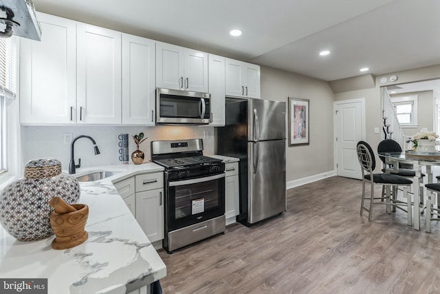 kitchen featuring appliances with stainless steel finishes, white cabinetry, backsplash, light hardwood / wood-style flooring, and sink