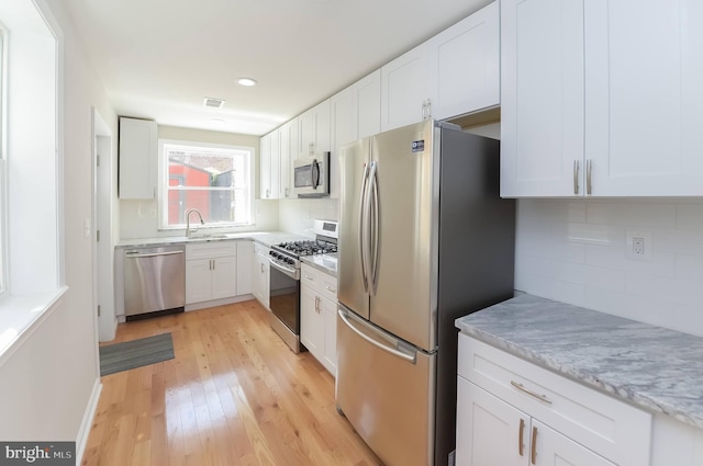 kitchen featuring light hardwood / wood-style floors, white cabinetry, light stone countertops, and stainless steel appliances