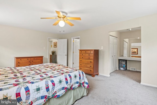 bedroom with built in desk, ceiling fan, light colored carpet, and a closet