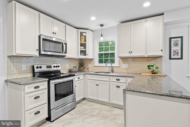 kitchen with hanging light fixtures, sink, white cabinetry, appliances with stainless steel finishes, and light stone countertops