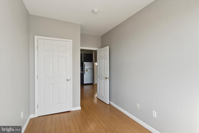 unfurnished bedroom with light hardwood / wood-style flooring and stainless steel fridge