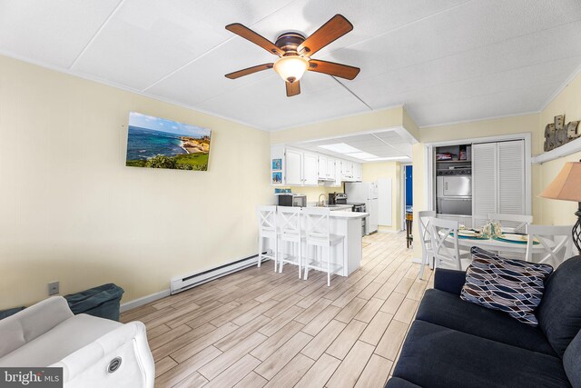 living room featuring a baseboard heating unit, light hardwood / wood-style floors, ceiling fan, and sink