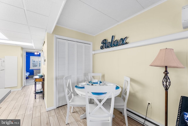 dining area with a paneled ceiling, light hardwood / wood-style floors, crown molding, and baseboard heating