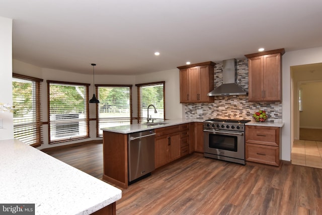 kitchen with wall chimney range hood, kitchen peninsula, appliances with stainless steel finishes, dark wood-type flooring, and decorative light fixtures