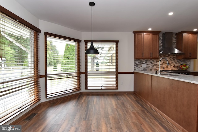 kitchen featuring wall chimney range hood, dark wood-type flooring, hanging light fixtures, sink, and tasteful backsplash