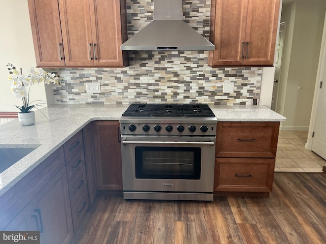 kitchen with decorative backsplash, wall chimney exhaust hood, stainless steel range, light stone countertops, and dark hardwood / wood-style flooring