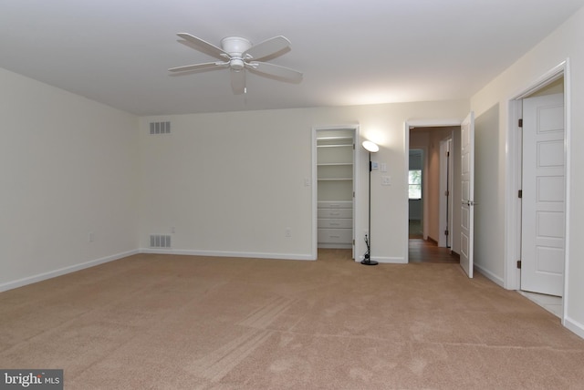 interior space featuring light carpet, a walk in closet, a closet, and ceiling fan