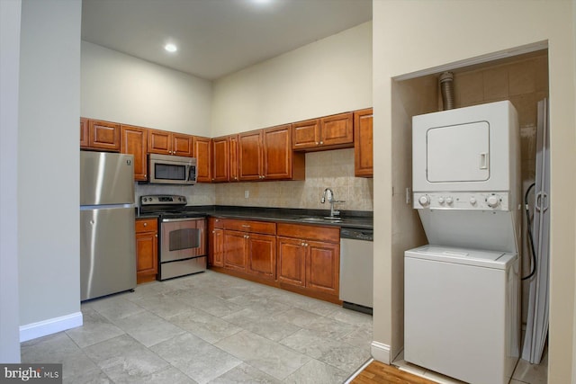 kitchen with appliances with stainless steel finishes, a towering ceiling, sink, and stacked washer / dryer