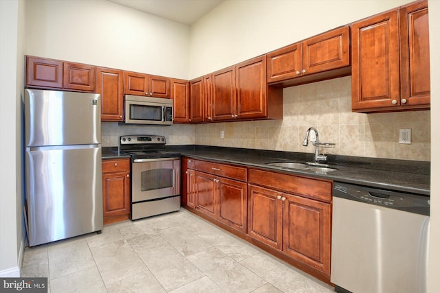 kitchen with decorative backsplash, a towering ceiling, light tile patterned floors, stainless steel appliances, and sink