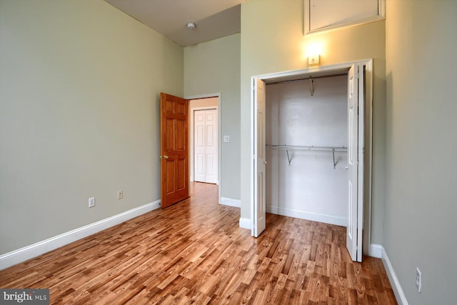 unfurnished bedroom featuring light wood-type flooring, a towering ceiling, and a closet