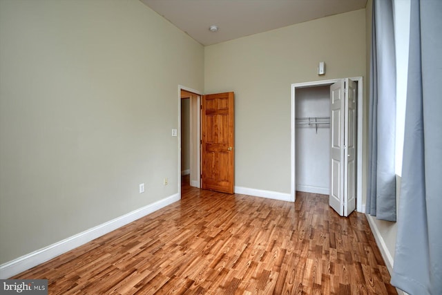 unfurnished bedroom featuring high vaulted ceiling, a closet, and light hardwood / wood-style floors