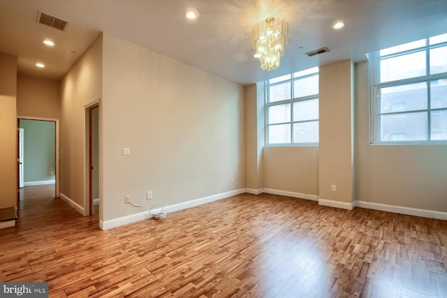 spare room featuring light hardwood / wood-style flooring, a chandelier, and a healthy amount of sunlight