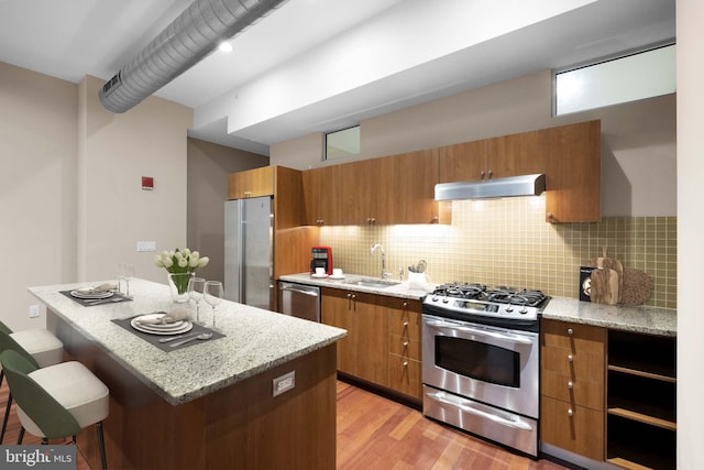 kitchen with a kitchen breakfast bar, light hardwood / wood-style floors, tasteful backsplash, stainless steel appliances, and sink