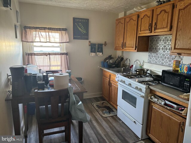 kitchen featuring sink, gas range gas stove, a textured ceiling, dark wood-type flooring, and decorative backsplash