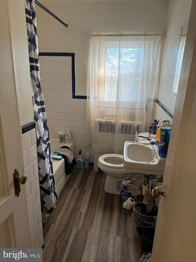 bathroom featuring radiator heating unit, tile walls, hardwood / wood-style flooring, shower / bath combo with shower curtain, and toilet