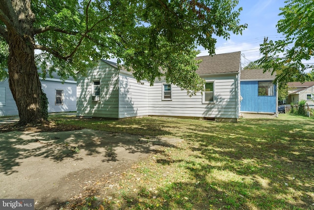 rear view of property featuring a lawn and a shingled roof