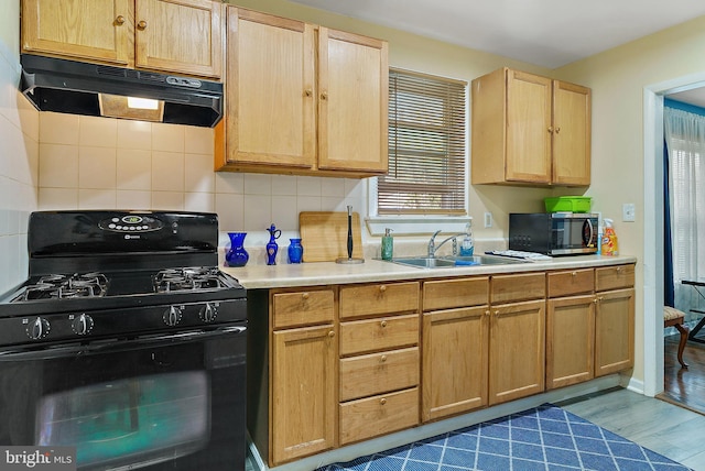 kitchen featuring light countertops, stainless steel microwave, black gas range, under cabinet range hood, and a sink