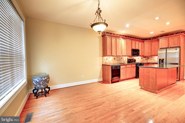 kitchen featuring hanging light fixtures, tasteful backsplash, a kitchen island, light hardwood / wood-style flooring, and black appliances