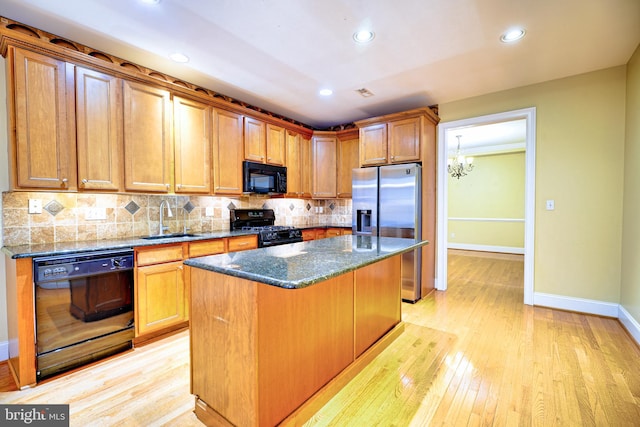 kitchen featuring sink, light hardwood / wood-style flooring, black appliances, a center island, and dark stone counters