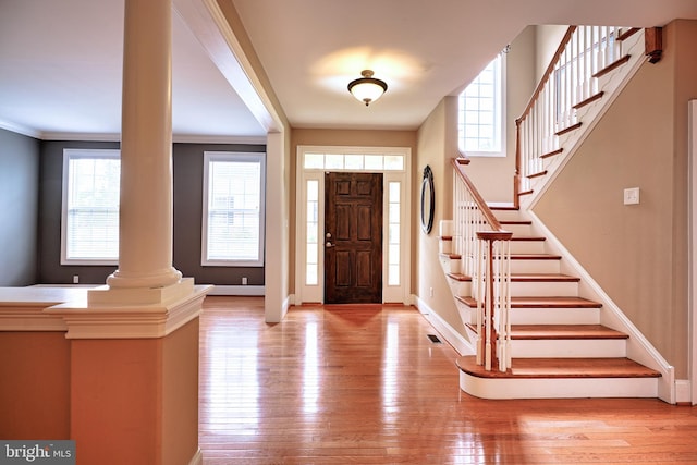 foyer with ornamental molding, light wood-type flooring, and decorative columns