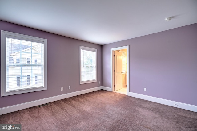 unfurnished bedroom with multiple windows, carpet flooring, and ensuite bathroom