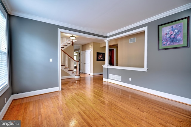 empty room with ornamental molding, decorative columns, and light hardwood / wood-style floors