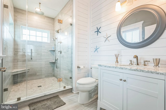 bathroom featuring wooden walls, vanity, toilet, and a shower with shower door