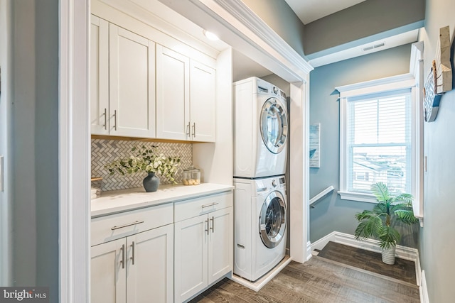 washroom featuring stacked washer / dryer, dark wood-type flooring, and cabinets