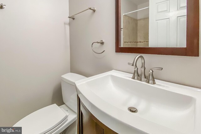 bathroom featuring a tile shower, vanity, and toilet