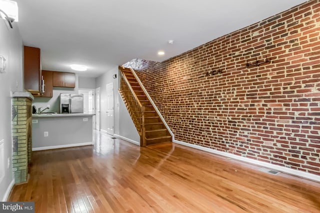 unfurnished living room featuring hardwood / wood-style flooring, sink, and brick wall