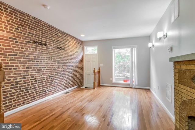 unfurnished living room with light wood-type flooring, brick wall, and a fireplace