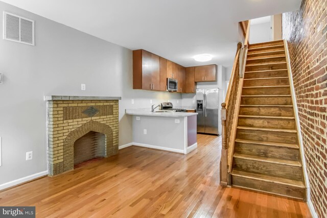 kitchen with light wood-type flooring, kitchen peninsula, stainless steel appliances, and brick wall