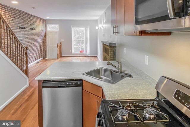 kitchen featuring light hardwood / wood-style floors, sink, stainless steel appliances, and brick wall