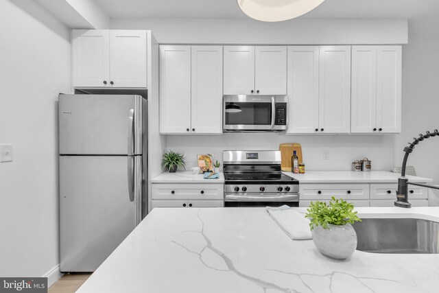 kitchen with light stone counters, white cabinetry, appliances with stainless steel finishes, and light hardwood / wood-style flooring