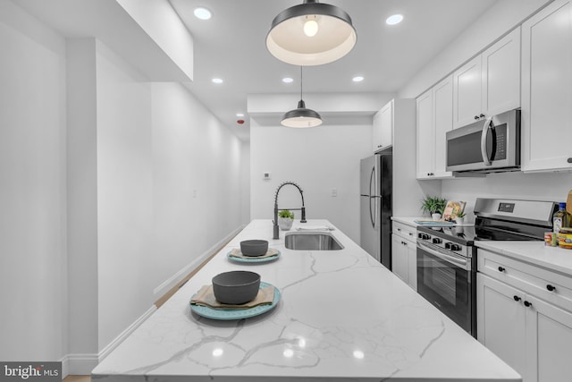 kitchen with light stone countertops, appliances with stainless steel finishes, sink, pendant lighting, and an island with sink