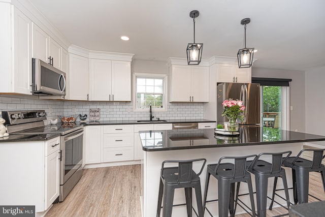 kitchen with appliances with stainless steel finishes, light hardwood / wood-style floors, white cabinetry, a center island, and sink