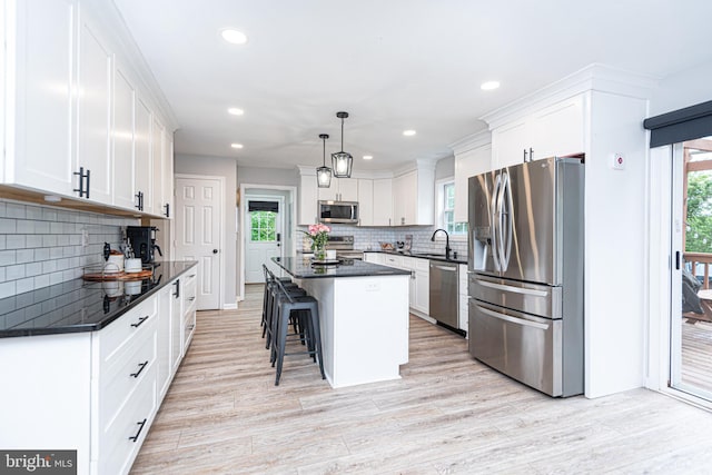 kitchen with decorative light fixtures, white cabinetry, stainless steel appliances, a center island, and light hardwood / wood-style floors