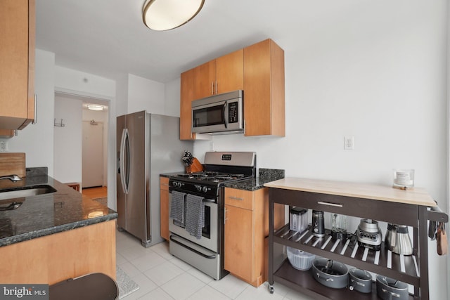 kitchen with dark stone countertops, appliances with stainless steel finishes, light tile patterned floors, and sink