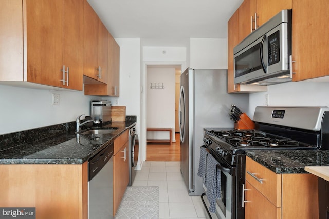 kitchen with washer / dryer, light tile patterned flooring, sink, stainless steel appliances, and dark stone countertops